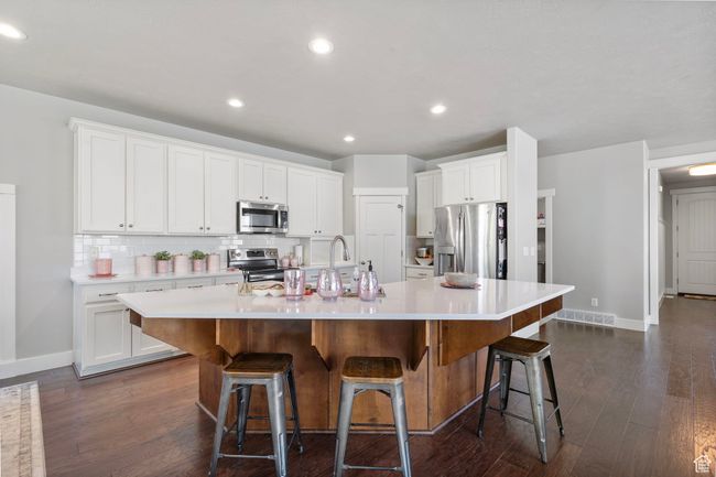 Kitchen with appliances with stainless steel finishes, a large island with sink, decorative backsplash, light countertops, and white cabinets | Image 9