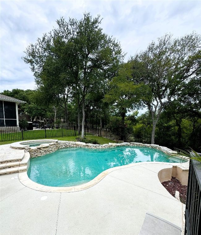 View of pool featuring a patio, a fenced backyard, a pool with connected hot tub, and view of scattered trees. | Image 34