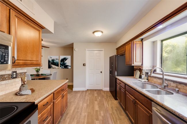 Kitchen featuring stainless steel appliances, tasteful backsplash, light wood-style flooring, light stone countertops, and brown cabinets | Image 4