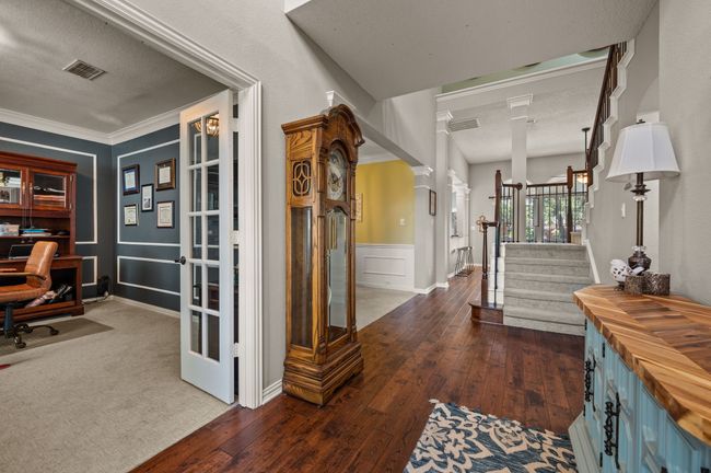 Hall with a textured ceiling, decorative columns, a desk, dark wood-style floors, and stairs | Image 7