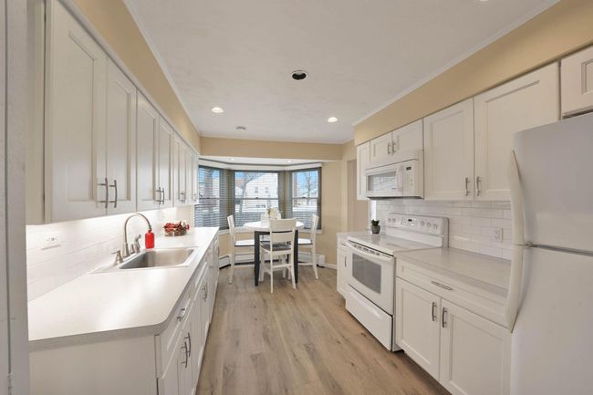 Kitchen featuring sink, white cabinets, white appliances, light wood-type flooring, and tasteful backsplash | Image 8
