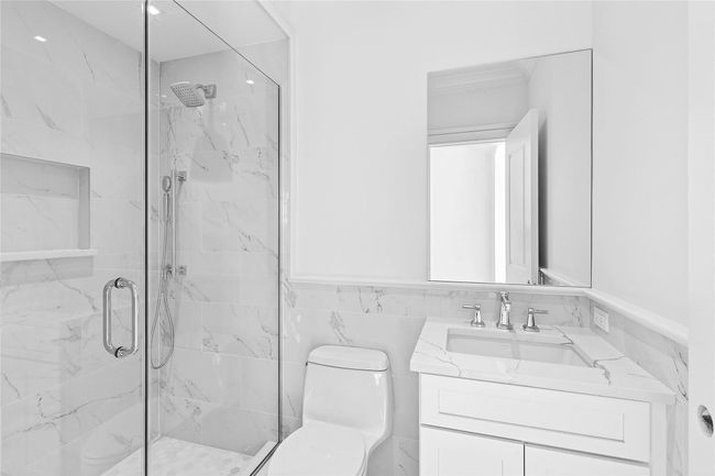 Bathroom featuring toilet, a marble finish shower, vanity, a wainscoted wall, and tile walls | Image 34