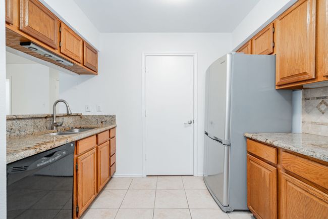 Kitchen featuring light stone counters, freestanding refrigerator, light tile patterned flooring, dishwasher, and a sink | Image 23