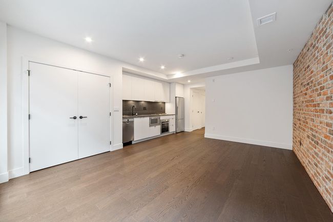 Unfurnished living room with brick wall, dark wood-style flooring, a tray ceiling, and recessed lighting | Image 21