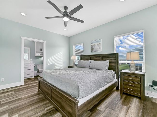 Escape to the serenity of this spacious master suite with attractive & easy-maintenance luxury vinyl plank flooring, coastal-inspired designer paint, abundant natural light, a lighted ceiling fan, recessed lights, balcony access, and a private en-suite bath. | Image 18