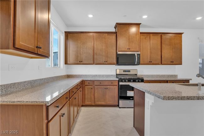Kitchen featuring brown cabinets, light stone countertops, a sink, and appliances with stainless steel finishes | Image 12