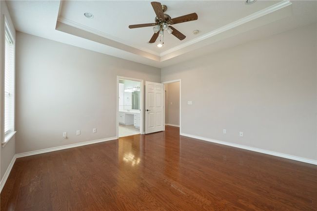 Spare room featuring a tray ceiling, crown molding, ceiling fan, baseboards, and wood finished floors | Image 18