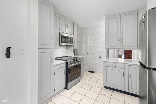 kitchen with light tile patterned flooring, visible vents, brick wall, light countertops, and appliances with stainless steel finishes | Image 21