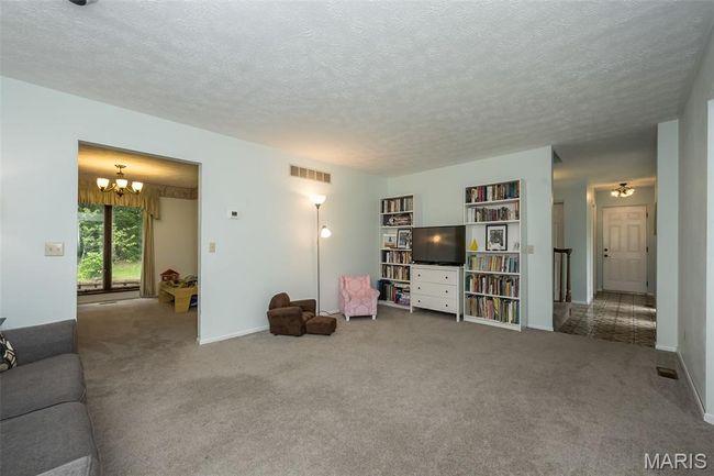 Carpeted living area featuring a chandelier, a textured ceiling, and baseboards | Image 6