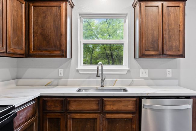 Kitchen with dishwasher, dark brown cabinets, stove, and light stone counters | Image 10