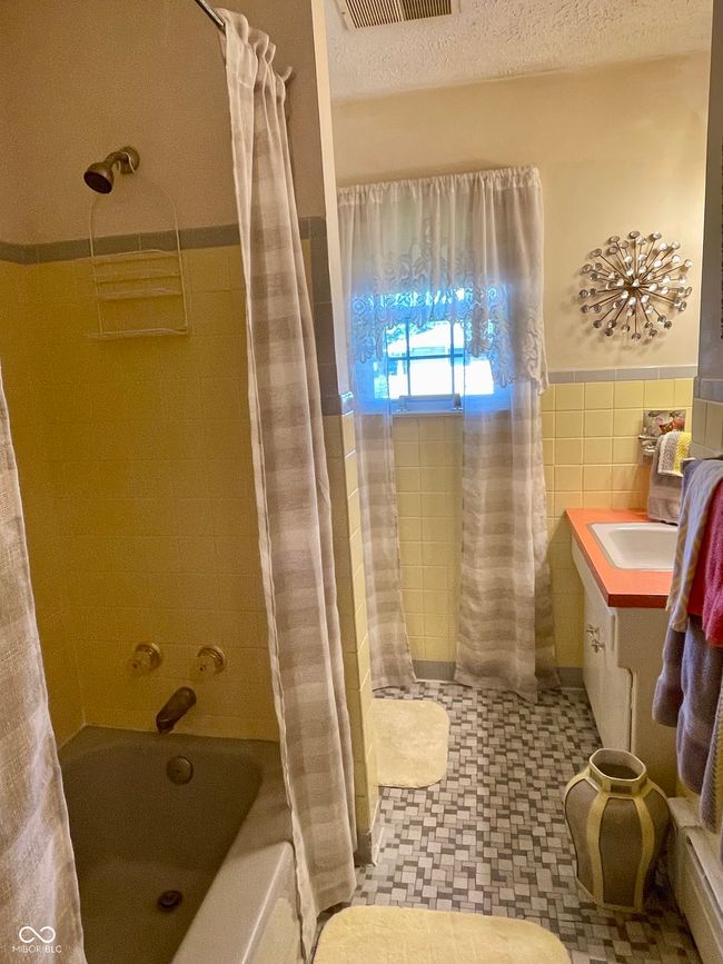Guest bath featuring shower / tub combo with curtain, wainscoting, tile walls, tile patterned floors, and vanity | Image 32