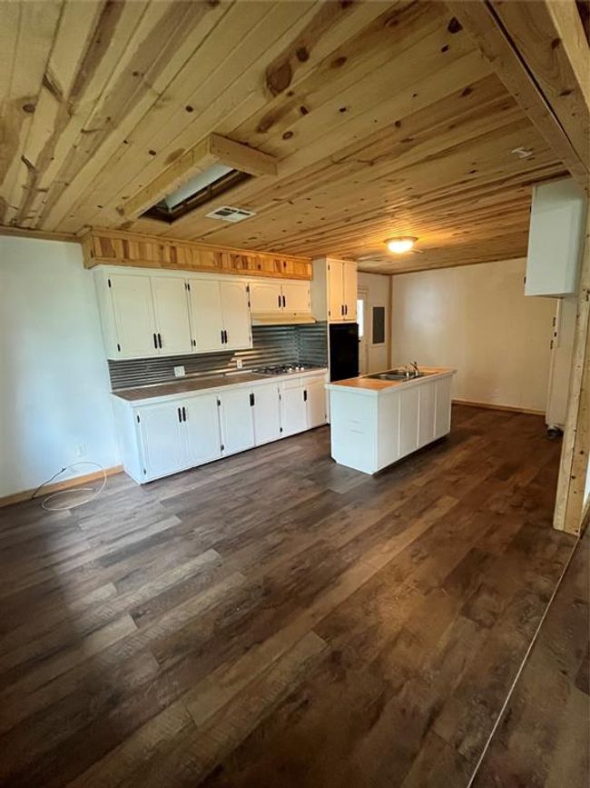 Kitchen with white cabinets, dark wood finished floors, and a center island with sink | Image 8