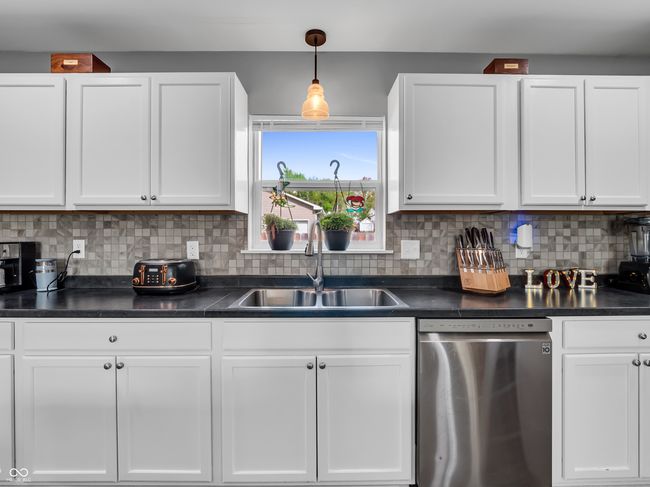 kitchen featuring white cabinetry, dark countertops, stainless steel dishwasher, and a sink | Image 7