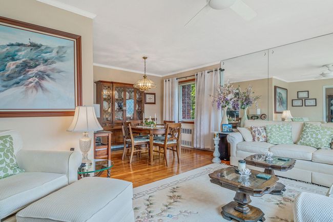 Living area with a ceiling fan, wood finished floors, ornamental molding, and radiator heating unit | Image 4