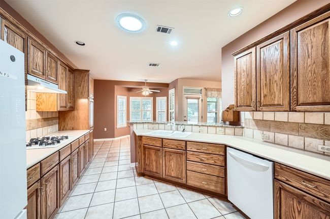 Kitchen with white appliances, a sink, under cabinet range hood, decorative backsplash, and light tile patterned floors | Image 11