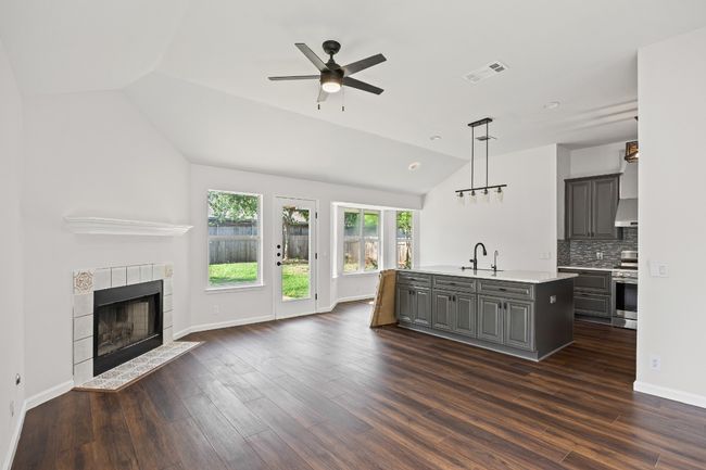 Unfurnished living room with vaulted ceiling, ceiling fan, a tile fireplace, and dark wood finished floors | Image 5