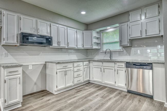 Kitchen with stainless steel dishwasher, black microwave, light wood finished floors, a textured ceiling, and white cabinets | Image 19