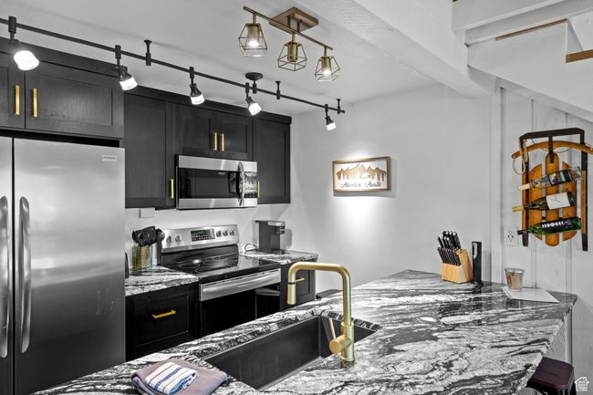 Kitchen featuring stainless steel appliances, dark cabinets, light stone countertops, and rail lighting | Image 5