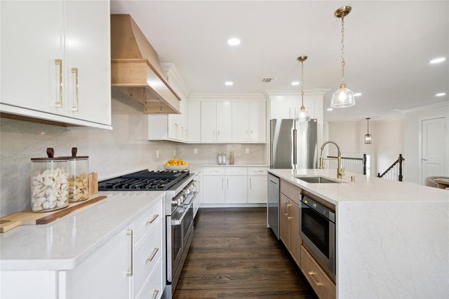 Kitchen featuring stainless steel appliances, premium range hood, decorative backsplash, pendant lighting, and white cabinets | Image 6