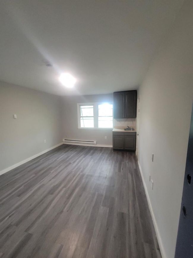 Unfurnished living room with a baseboard radiator, dark wood-style flooring, baseboards, and a sink | Image 23