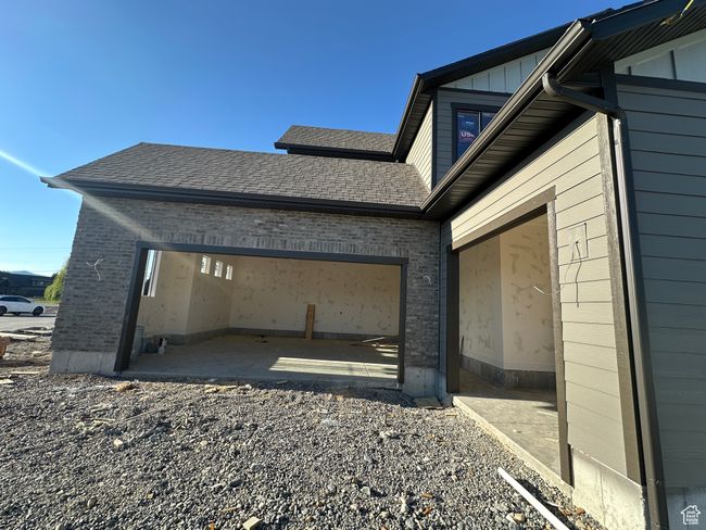 View of side of property featuring brick siding, a garage, roof with shingles, driveway, and board and batten siding | Image 35