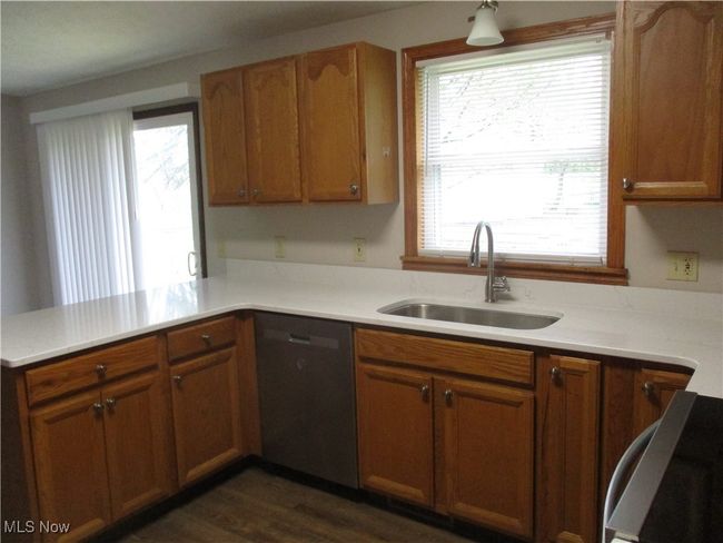 Kitchen with stove, light countertops, dishwasher, a sink, and a peninsula | Image 5