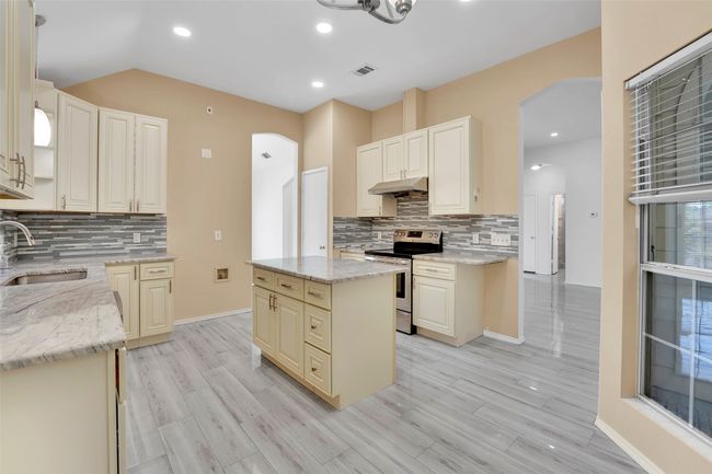Kitchen with light stone counters, a kitchen island, sink, tasteful backsplash, and stainless steel electric stove | Image 8