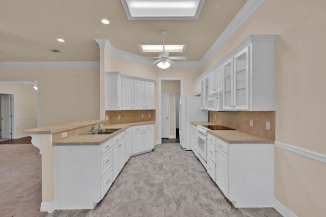 Kitchen with white appliances, a peninsula, white cabinets, light countertops, and ornamental molding | Image 8