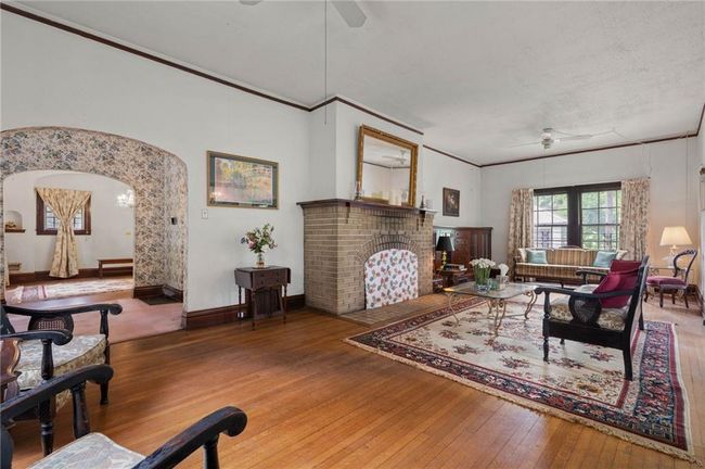 Living room featuring a ceiling fan, hardwood flooring, arched walkways, crown molding, brick fireplace, and beautiful built-in bookcase. | Image 5