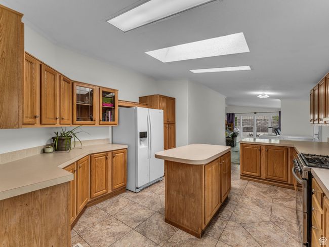 Kitchen featuring white fridge with ice dispenser, gas range, a skylight, a center island, and glass insert cabinets | Image 10