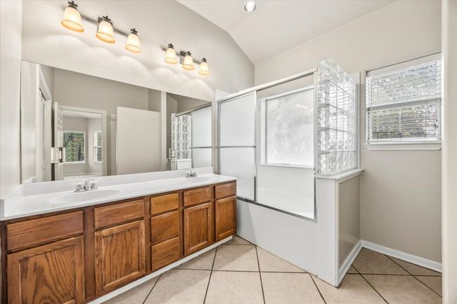 Full bathroom featuring tile patterned flooring, vaulted ceiling, a sink, and a healthy amount of sunlight | Image 17