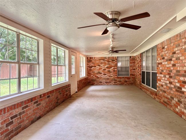 Unfurnished sunroom with brick wall, concrete flooring, a textured ceiling, and ceiling fan | Image 29