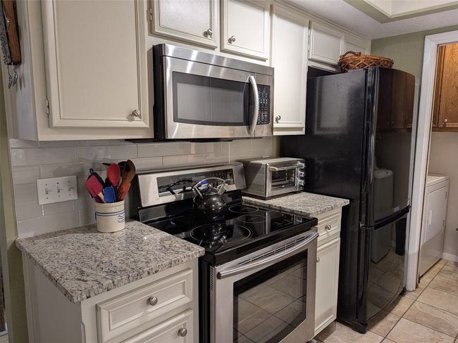 Kitchen with stainless steel appliances, backsplash, white cabinetry, light stone counters, and light tile patterned floors | Image 15