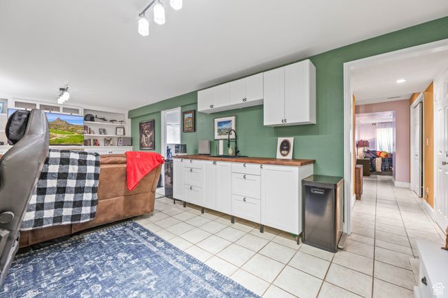 Kitchen featuring wooden counters, light tile patterned flooring, a sink, and white cabinetry | Image 29