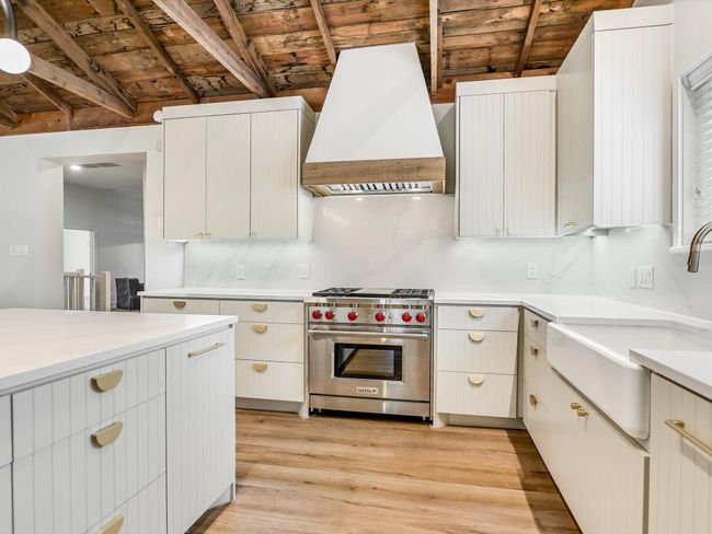 Kitchen with designer range, custom exhaust hood, light wood finished floors, light countertops, and a sink | Image 4