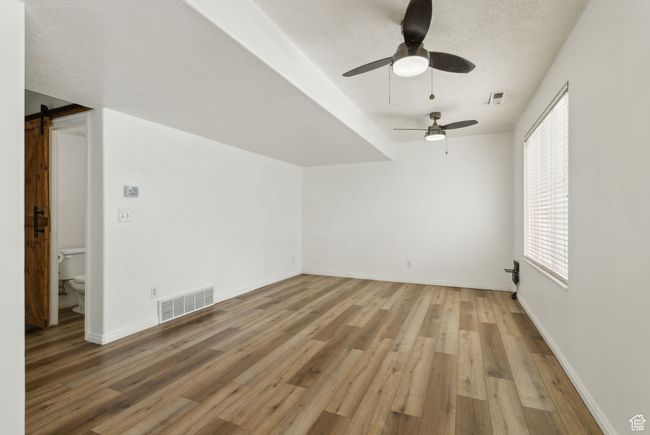 Additional living space featuring light wood-style flooring, a ceiling fan, a barn door, and baseboards | Image 8