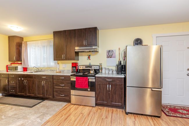 Kitchen with appliances with stainless steel finishes, under cabinet range hood, dark brown cabinets, and light wood-style flooring | Image 23