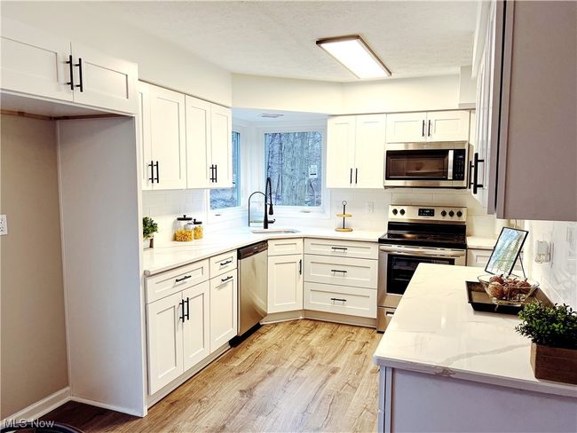 Kitchen with white cabinets, light hardwood / wood-style flooring, stainless steel appliances, and backsplash | Image 4
