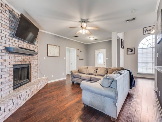 Living room with ceiling fan, wood finished floors, plenty of natural light, a brick fireplace, and ornamental molding | Image 9