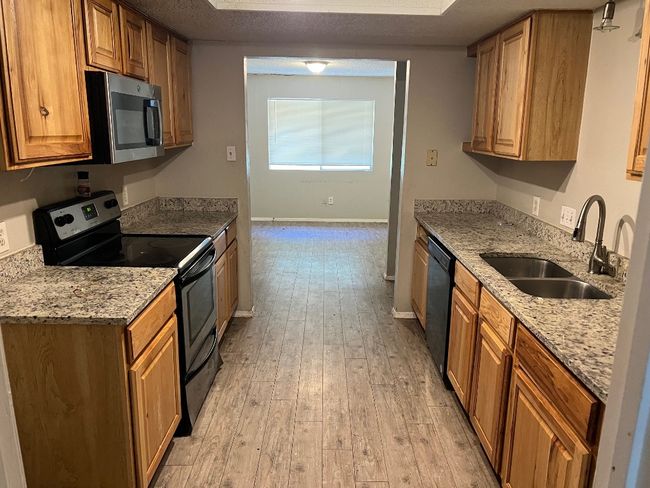 Kitchen with black range with electric cooktop, a sink, dishwasher, light wood finished floors, and baseboards | Image 5