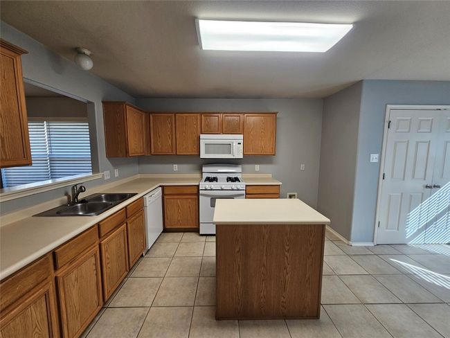 Kitchen with white appliances, a center island, brown cabinetry, light countertops, and light tile patterned flooring | Image 11