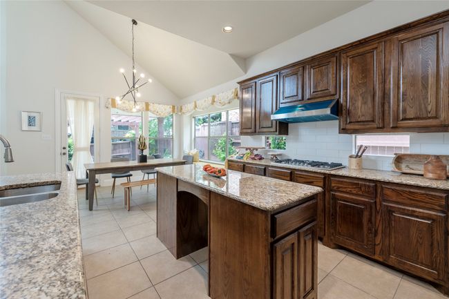 Kitchen featuring exhaust hood, a center island, lofted ceiling, light tile patterned flooring, and stainless steel gas stovetop | Image 13