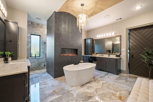 This luxurious bathroom features a freestanding tub, a modern fireplace, and elegant marble flooring. It includes dual vanities, a large mirror, and a stylish chandelier, creating a spa-like atmosphere. | Image 30