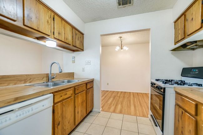 Kitchen with white dishwasher, gas range oven, a sink, light tile patterned floors, and a textured ceiling | Image 11