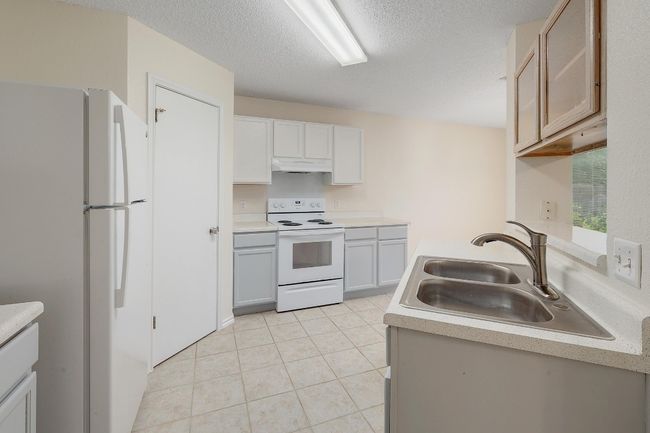 Kitchen with white appliances, under cabinet range hood, a sink, light countertops, and light tile patterned floors | Image 11