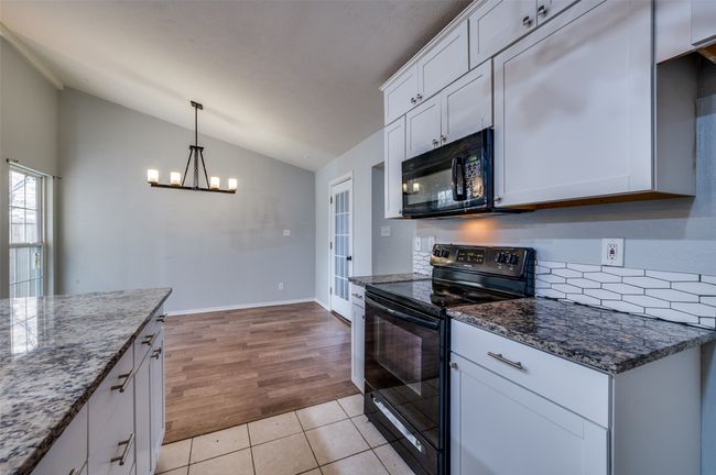 Kitchen featuring black appliances, lofted ceiling, a chandelier, dark stone countertops, and white cabinets | Image 8