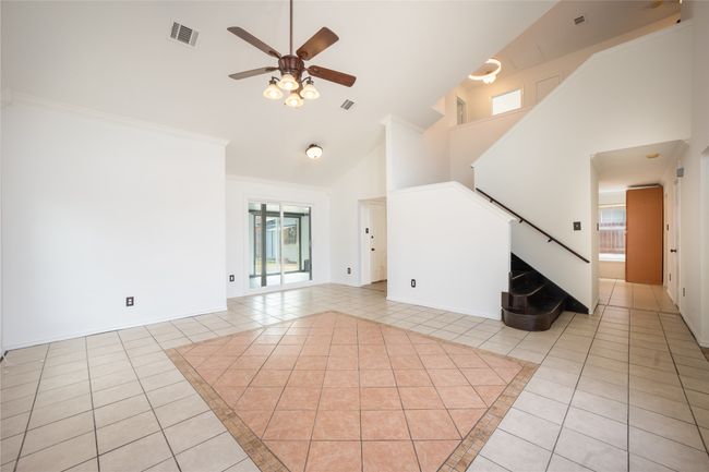 Unfurnished living room featuring stairway, light tile patterned floors, high vaulted ceiling, ceiling fan, and visible vents | Image 4
