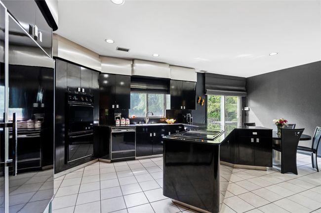 Kitchen with black appliances, dark cabinets, light tile patterned floors, recessed lighting, and dark countertops | Image 10