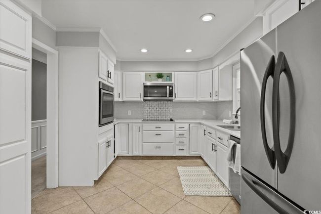 Kitchen featuring stainless steel appliances, a sink, crown molding, decorative backsplash, and white cabinets | Image 16