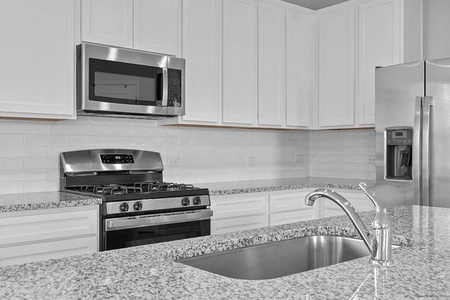 Kitchen with appliances with stainless steel finishes, white cabinets, decorative backsplash, and light stone counters | Image 10